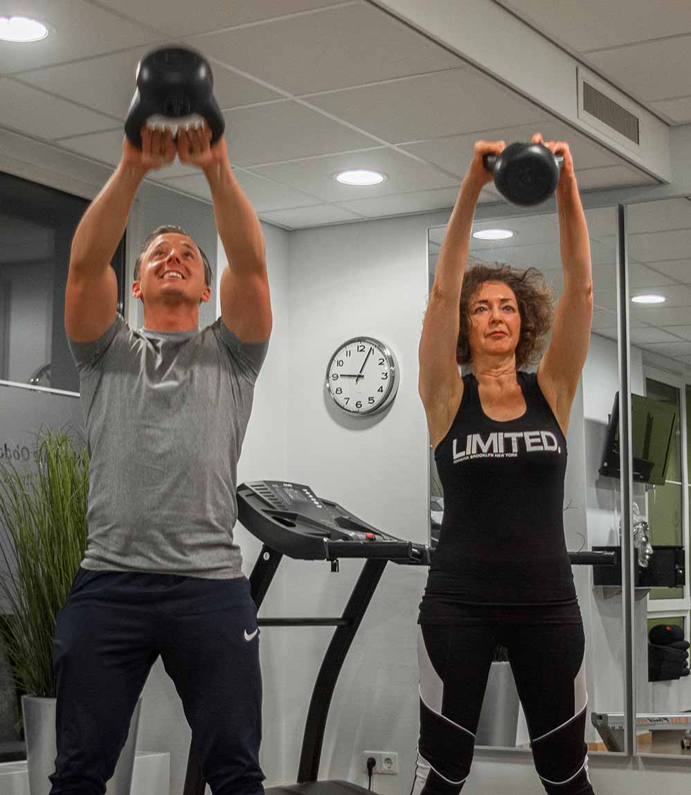 Twee patiënten trainen met een kettlebell in de oefenzaal van Duif Fysiotherapie