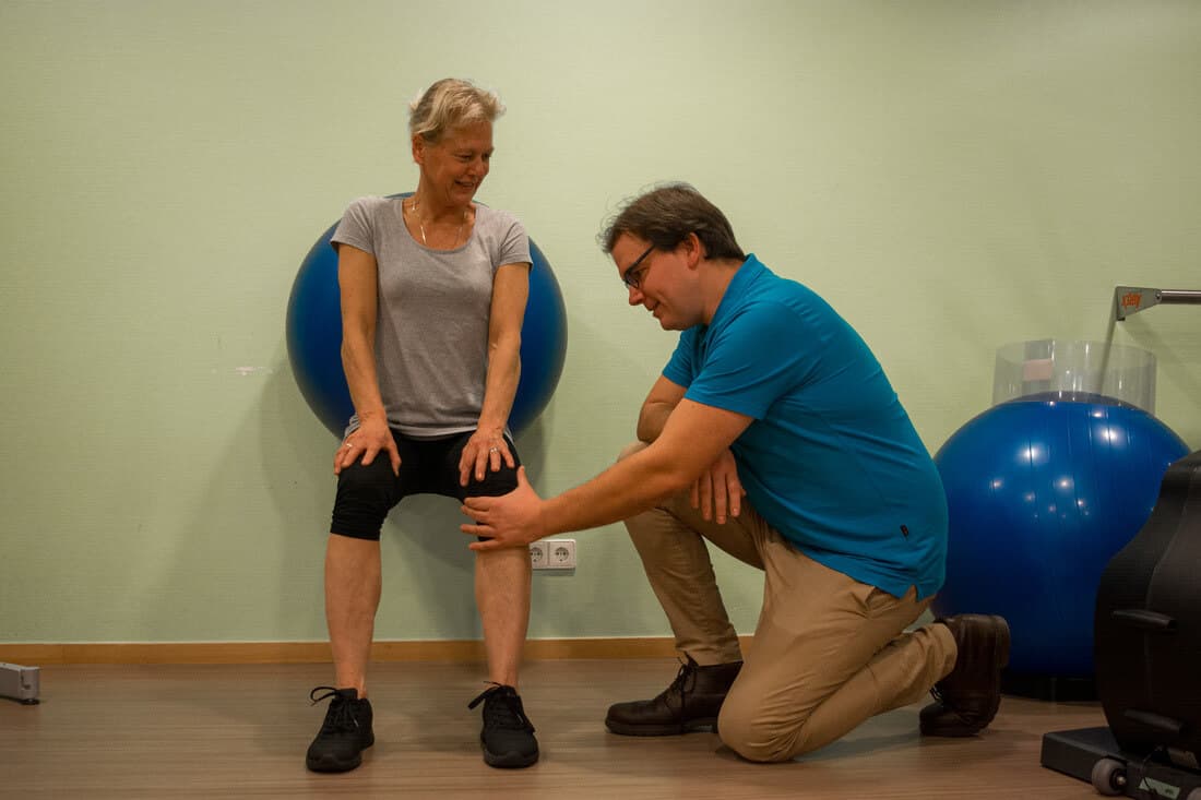 Fysiotherapeut controleert de knie van een patiënte die met een bal tegen de muur een squat doet